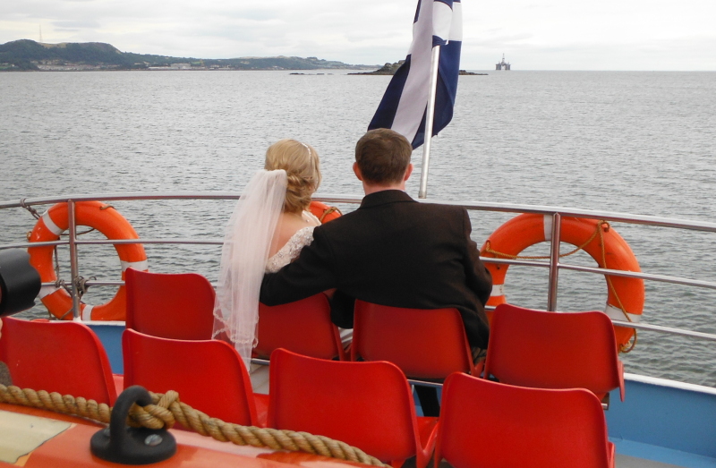  the bride and groom sitting at the back of the boat looking back to Inchcolm 